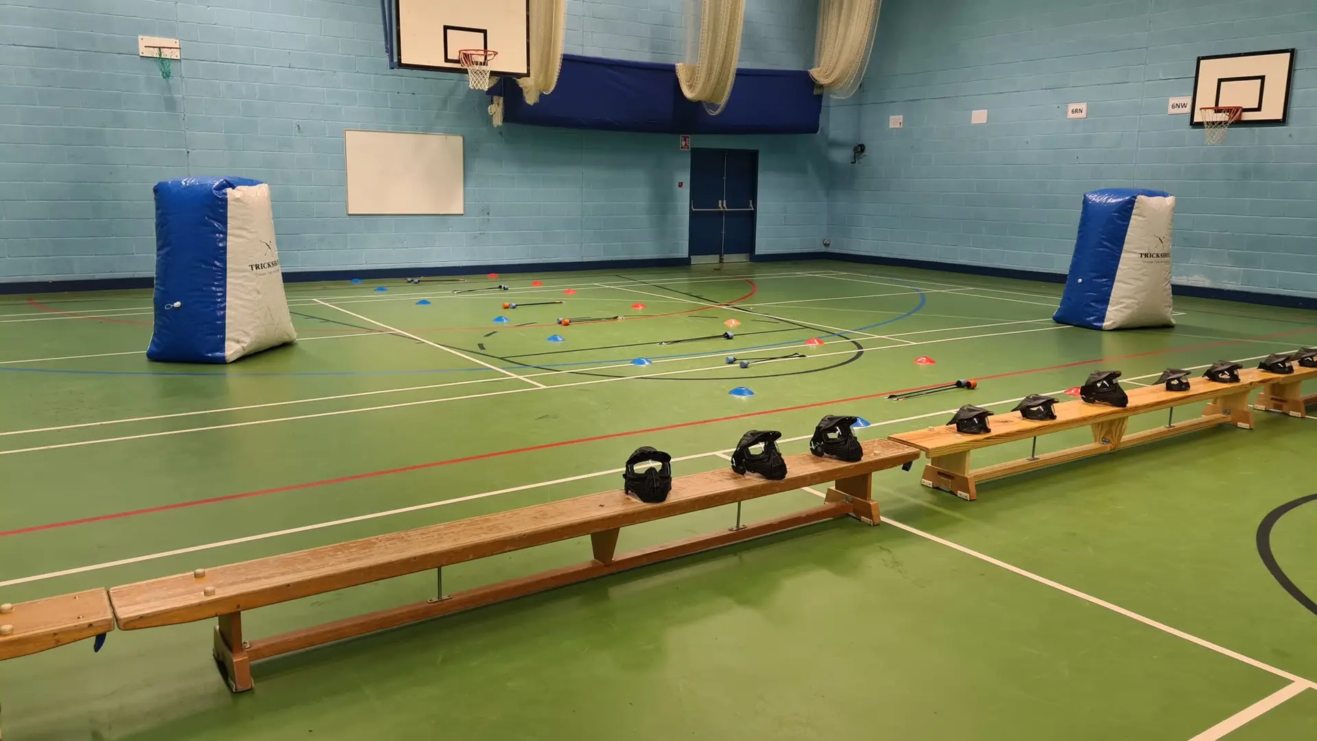 An empty sports hall set up for a game: bunkers, cones and masks lined up on a bench