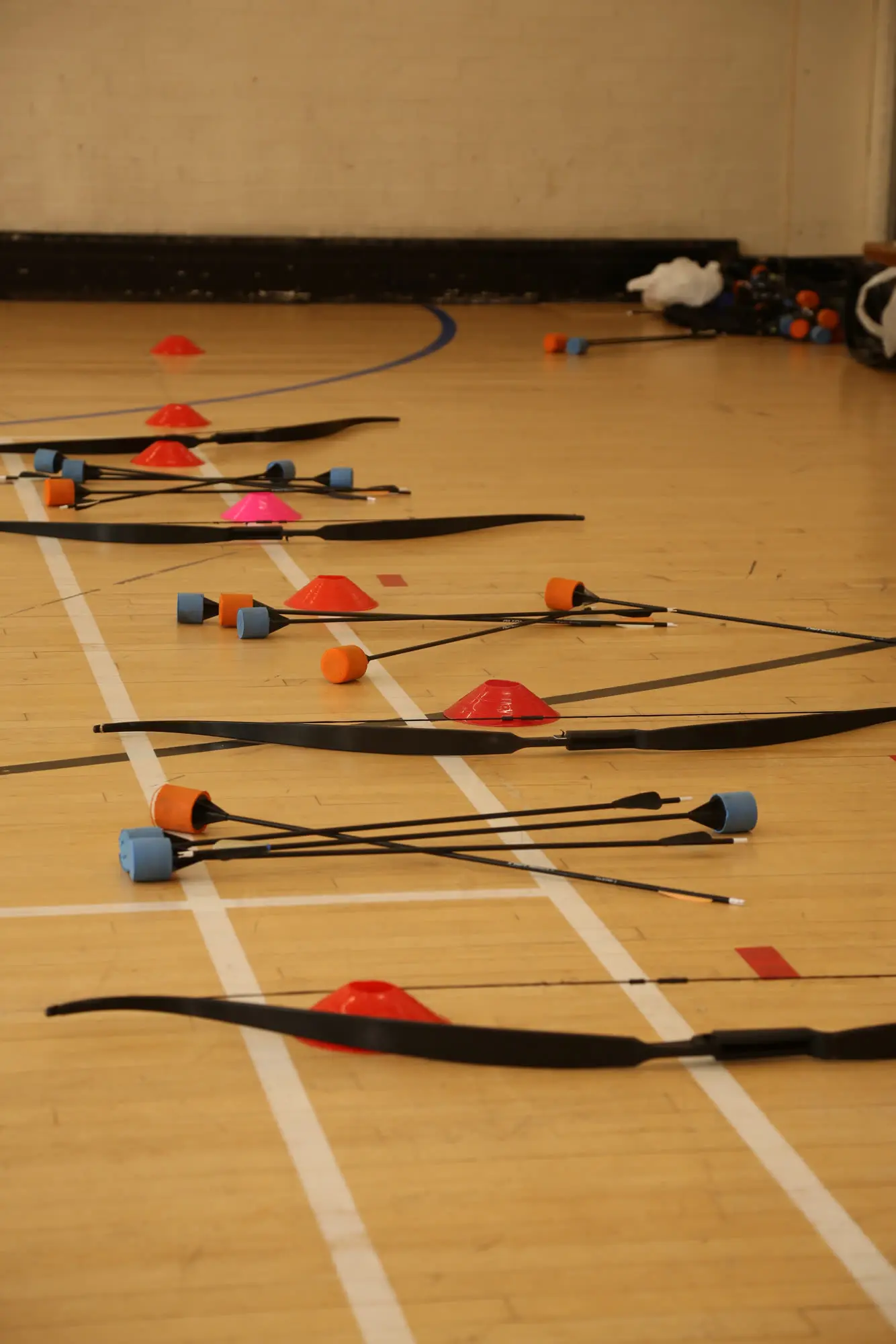 Bows and orange and blue foam-tipped arrows laid out on a hall floor