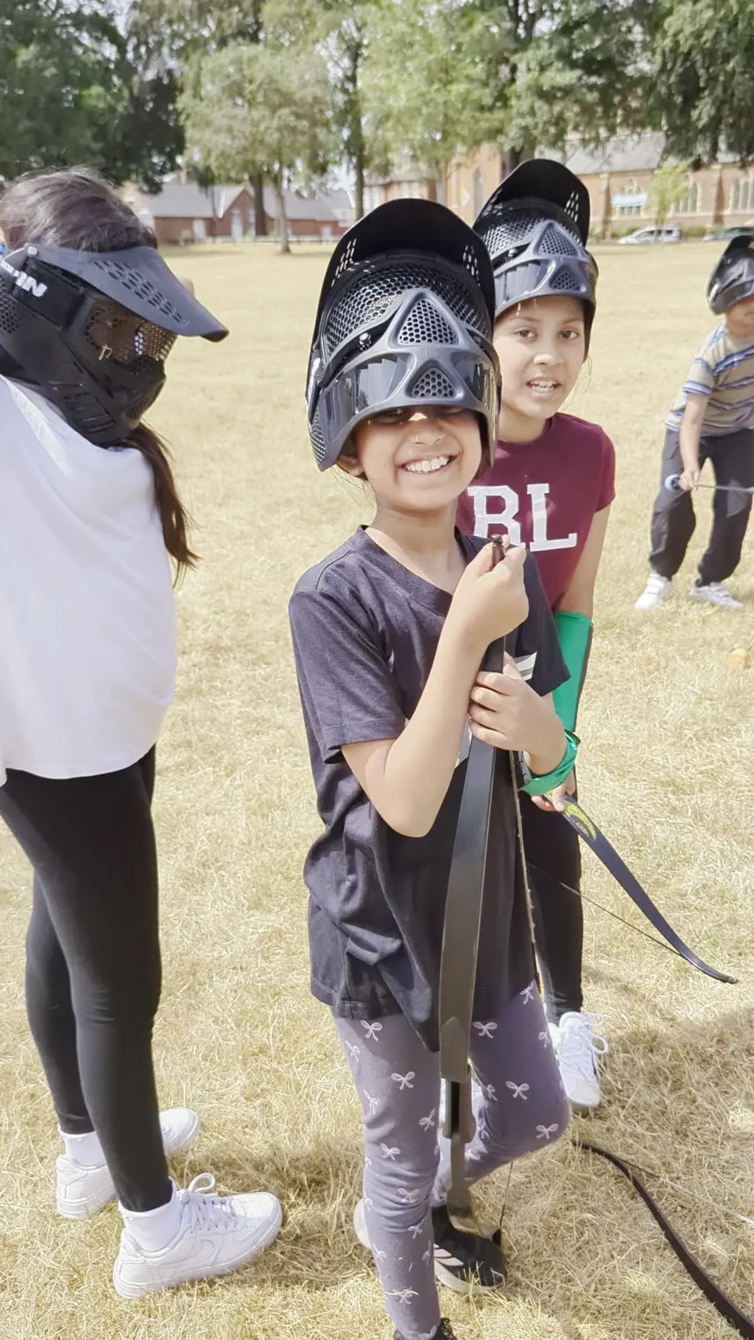 Two children in masks and arm guards smile with their bows at an outdoor session