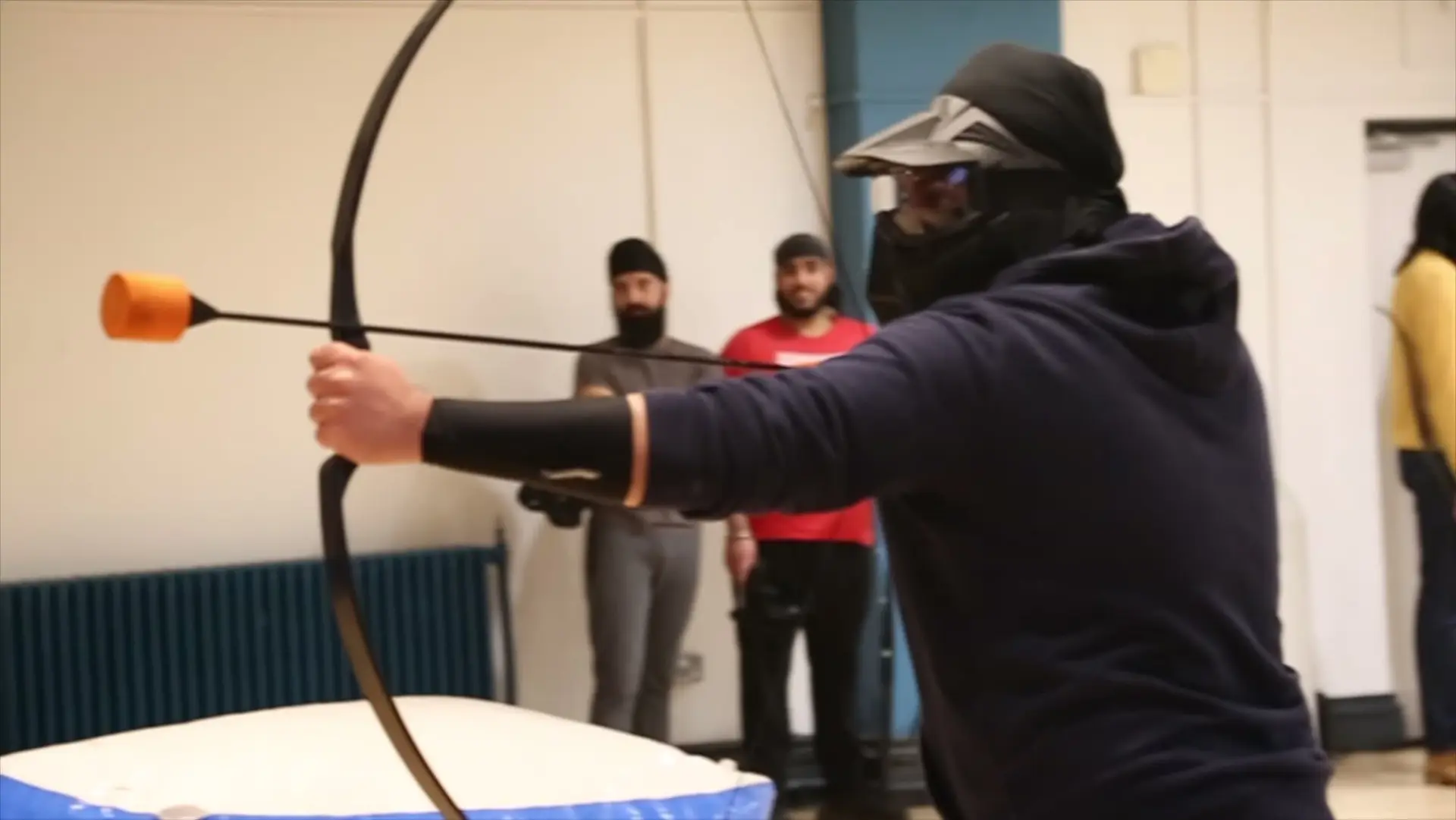 A masked player aims a foam-tipped arrow across the hall